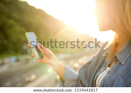 girl taking pictures of a landscape, close-up of a phone in her hand at sunset