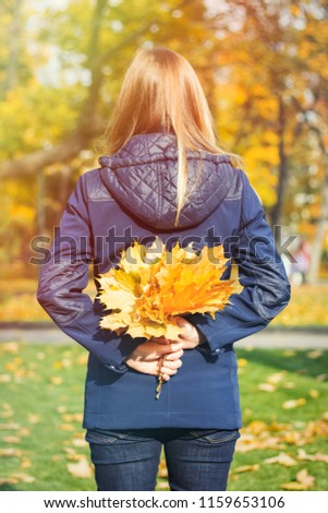 Young girl holds a yellow autumn leaves in her hands behind her 