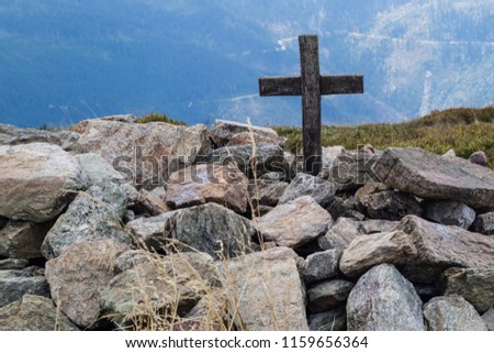Cross on the top of a mountain in central europe. A wooden sign of Christianity lined with stones. Season of the summer.