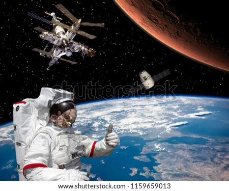 Astronaut shows the thumbs-up about flying to Mars. Space station on the backdrop.  Space craft in outer space.. The elements of this image furnished by NASA.
