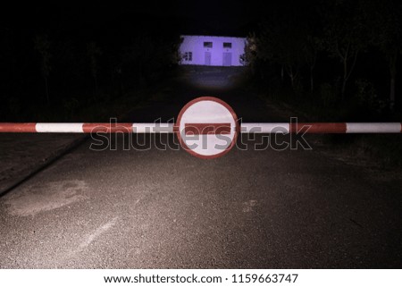 Wrong way concept. Barrier with sign no entry at night. Barrier standing on road to the scary haunted building with ghosts or maniac. Warning about the danger zone