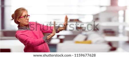Beautiful adult blonde woman signaling stop with both palms of hands facing forward, with a serious and stern expression, forbidding. Mid-lateral view.