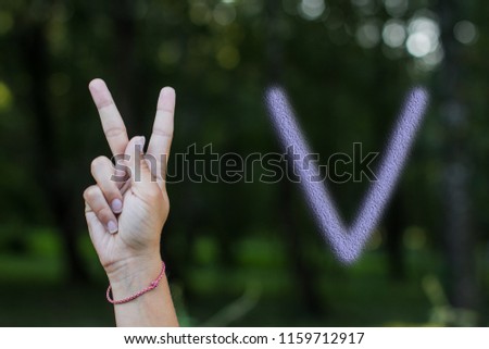 non verbal people communication concept of dactyl alphabet by person hand with letter "V" on unfocused blurred dark natural background environment 
