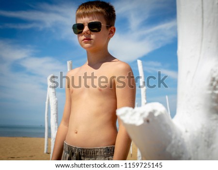 Young caucasian boy, wearing camo pants and sun glasses, at the beach on the Adriatic Sea, Italy