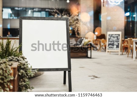 Close up of blank light sandwich board at the street next to restaurant.