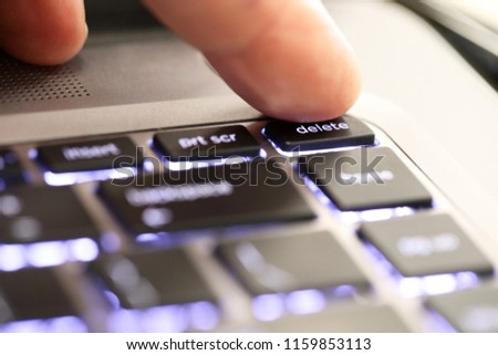 close up of a finger hitting pushing the delete symbol button tab on an illuminated laptop computer key board. The delete key