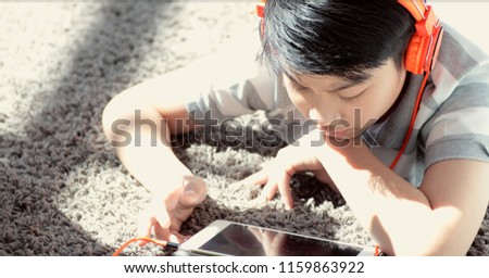 Happy asian boy Lying On Carpet Playing Game On Digital Tablet At Home