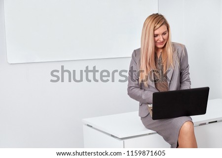Business woman in gray suit, sitting on desk and working on laptop