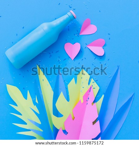 Painted in deep blue beer or cocktail bottle lies among hearts and palm tropical leaves made of paper. Summer vacation party concept