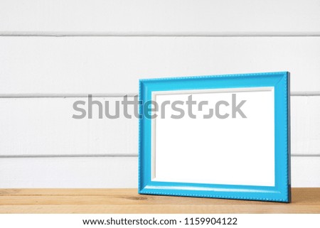Blue picture frame put on wooden table in white wood wall room.