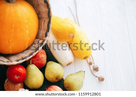 Happy Thanksgiving. Pumpkin and zucchini in stylish straw basket with apples and pears on white wooden background in light, Space for text. Fall Harvest and hello autumn concept