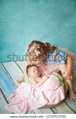 Beautiful blond girl hugging her sleeping newborn sister, beautiful sisters