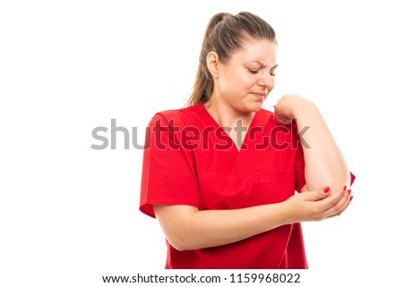 Portrait of young medical nurse wearing red scrub showing elbow pain gesture isolated on white background with copyspace advertising area