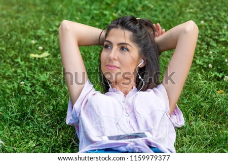 Young Woman with Earphones  Listening to Music on a Smartphone in the Park 