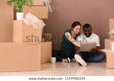 Interracial couple sitting on floor with boxes and laptop. Moving into new house