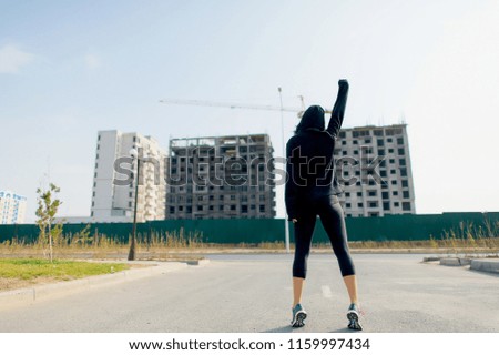 A woman in a black sweatshirt against the background of high-rise buildings. Girl sportsman on the background of buildings