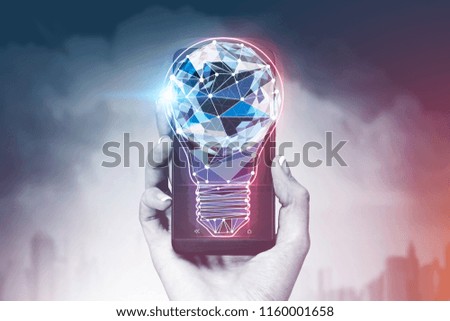 Woman hand holding a smartphone with a glowing polygonal light bulb on the screen. A city and a cloudy sky background. Toned image double exposure mock up. Shades of gray