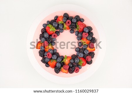 Cake with whipped pink cream, fresh strawberries, blueberries, blackberry and raspberry on white background. Top view. Picture for a menu or a confectionery catalog.