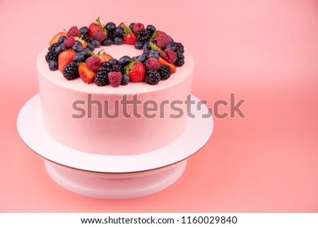 Cake with whipped pink cream, fresh strawberries, blueberries, blackberry and raspberry on pink background. Picture for a menu or a confectionery catalog.
