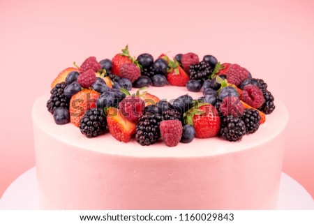 Cake with whipped pink cream, fresh strawberries, blueberries, blackberry and raspberry on pink background. Close up. Picture for a menu or a confectionery catalog.
