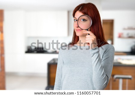 Young redhead girl taking a magnifying glass and looking through it on unfocused background
