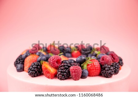 Cake with whipped pink cream, fresh strawberries, blueberries, blackberry and raspberry on pink background. Close up. Picture for a menu or a confectionery catalog.