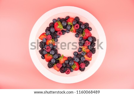 Cake with whipped pink cream, fresh strawberries, blueberries, blackberry and raspberry on pink background. Top view. Picture for a menu or a confectionery catalog.