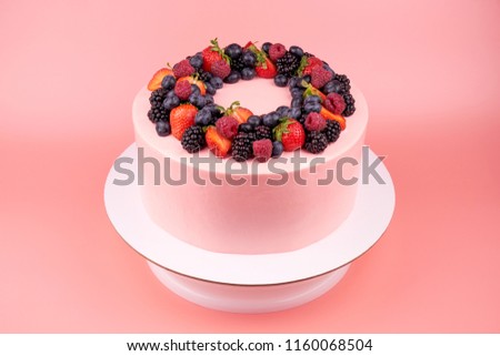 Cake with whipped pink cream, fresh strawberries, blueberries, blackberry and raspberry on pink background. Picture for a menu or a confectionery catalog.