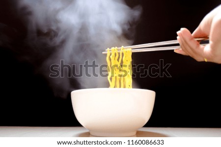 hand holding chopsticks of instant noodles with steam and smoke in bowl black backdrop. selective focus