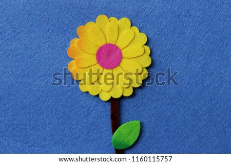 Yellow felt flower with green leaf on blue fabric background.

