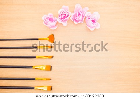 Flat lay photography. Rose flowers and brushes on a wooden table desk. Top point of view. Artist idea concept.