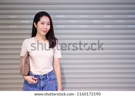 Asian woman is smiling and standing in front of the grey steel door.