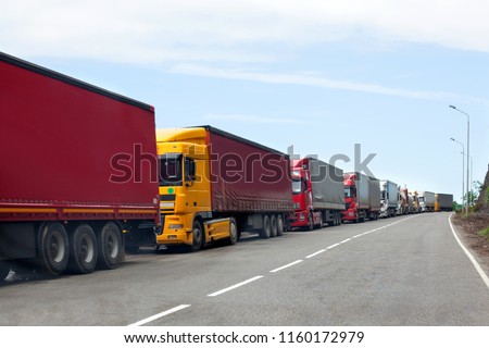 Queue of trucks passing the international border, red and different colors trucks in traffic jam on the road Royalty-Free Stock Photo #1160172979