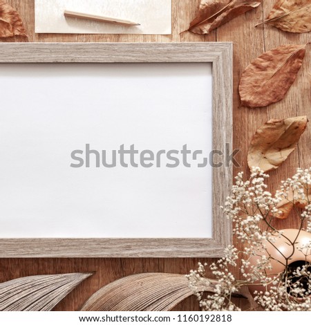 A square photo of an empty mockup frame on an autumn desk with leaves, white flowers, old envelopes and dried decoration