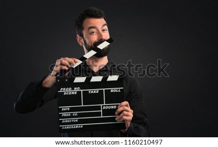 Handsome man with beard holding a clapperboard on black background
