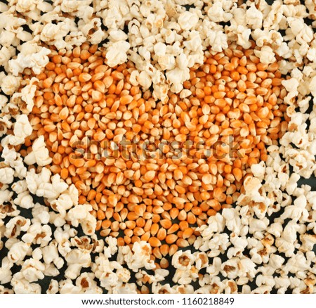 Heart made of delicious popcorn and kernels on table