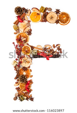 Letter "F" made of Christmas spices, dry orange and apple slices and small gifts. Isolated on white background