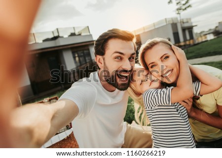Optimistic unshaven male doing selfie with cheerful woman and pleased child. Glad kid hugging beaming mom