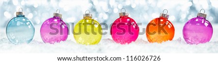 Colourful translucent Christmas baubles arranged in a row in snow against sparkling party ligts suitable as a banner or border