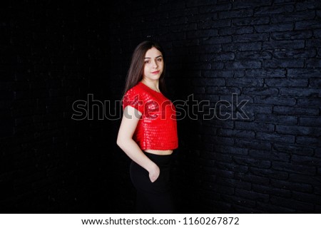 Portrait of a beautiful brunette girl in red t-shirt and black trousers next to the brick wall in the studio.