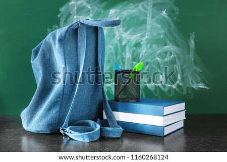 Backpack, books and scissors on table near chalkboard with erased text BACK TO SCHOOL