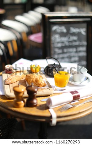 breakfast table set outside a cafe / restaurant. French / English stile breakfast with coffee or tea menu. fresh bread and croissants for breakfast with orange juice on a sunny morning. 