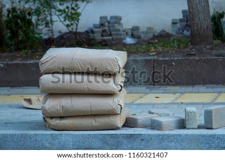 Four Paper bags with cement are stacked on the sidewalk. Building materials for the construction of sidewalk and footpaths. Cement in paper bags for the construction of pedestrian paths. Royalty-Free Stock Photo #1160321407