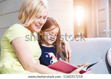 Happy mother and daughter sitting on the sofa in the modern house and looking intresting pictures in the colorfull book