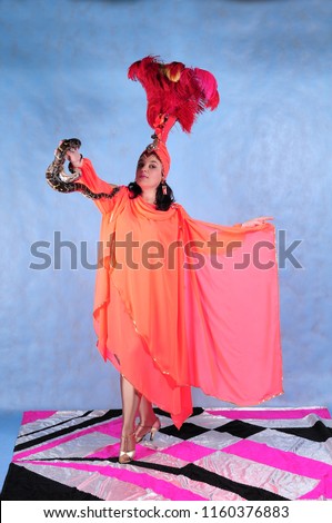 Animator woman with snake Python in pink dress with feathers on head on blue background