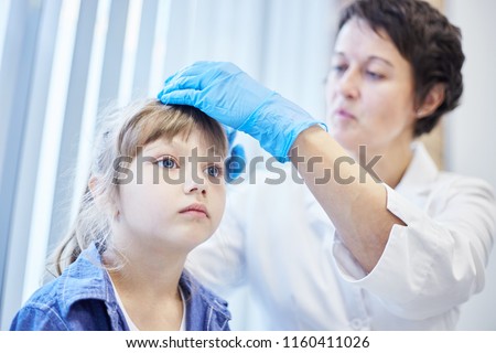 From below shot of female doctor in gloves checking hair and head of little girl in hospital