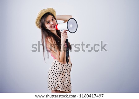 Portrait of a gorgeous young girl in swimming suit and hat talks into megaphone in studio.