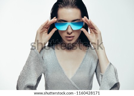 Funky fashion portrait of female model wearing silver outfit and blue mirrored sunglasses. Futuristic female model posing in studio.