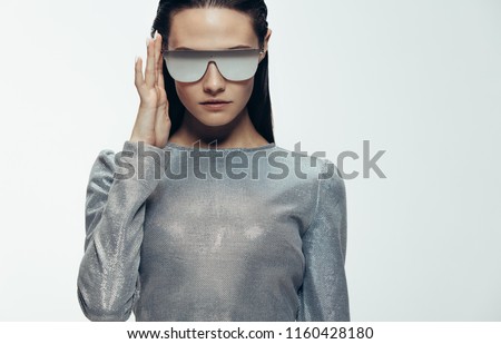 Close up portrait of woman in sliver outfit and mirrored sunglasses looking at camera. Stylish female model in robotic look against grey background.