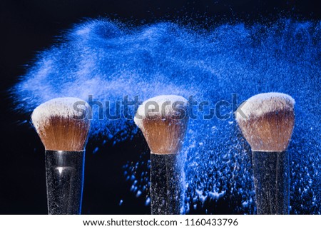 Make up, beauty and mineral cosmetics concept - powder brush on black background with blue powder splashed on it